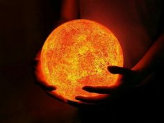 a person holding a glowing orange ball in their hands with the light shining on them