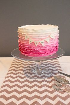 a pink and white cake sitting on top of a glass plate next to silverware