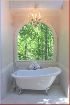 a white bath tub sitting under a window next to a chandelier