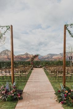 an outdoor wedding ceremony setup with wooden chairs and flowers on the aisle, in front of mountains