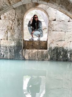 a woman sitting on the edge of a stone wall next to a body of water