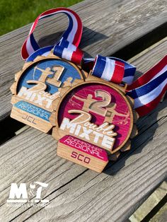 two medals sitting on top of a wooden bench next to each other with ribbons around them