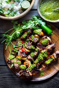 a plate filled with meat and veggies on skewers next to some herbs