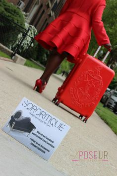 a woman in a red dress pulling a suitcase down the street with her hand on top of it