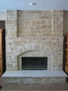 a stone fireplace in the middle of a living room with carpeted flooring and cabinets