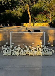 an outdoor sculpture with white flowers in the foreground and trees in the back ground