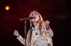 a woman standing in front of a microphone with her hands up and singing into the air