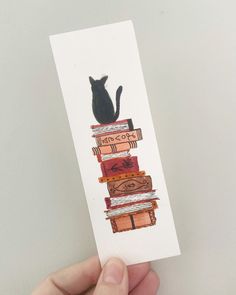 a person holding up a card with a cat on top of books in front of a white wall