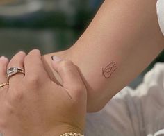 a woman's arm with a small tattoo on her left wrist and a diamond ring in the other hand