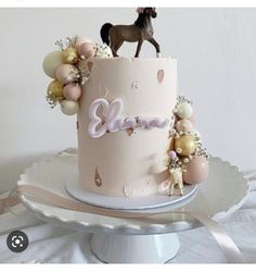 there is a pink cake with a horse on top and balloons around the edges that spell it's name