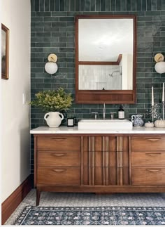 a bathroom with green tiled walls and wooden cabinetry, two sinks and a large mirror on the wall