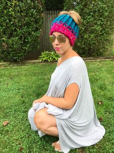 a woman sitting on the grass wearing sunglasses and a knitted headband in front of her face