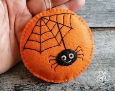 a hand holding an orange ornament with a spider on it's web