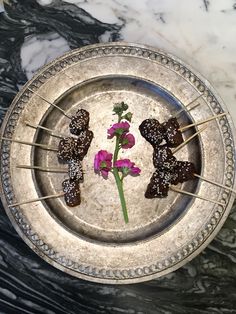 some food on skewers are sitting on a silver plate with flowers in it