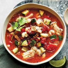 a bowl of soup with shrimp, zucchini and other vegetables on the side