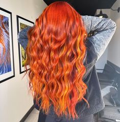 a woman with red and orange hair is looking at pictures on the wall behind her