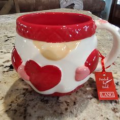 a red and white coffee mug with hearts on it sitting on a table next to a tag