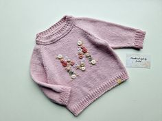 a pink sweater with flowers on it and a name tag attached to the front, sitting on a white surface