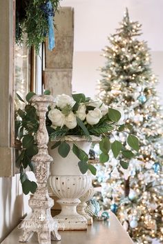 a white vase filled with flowers sitting on top of a table next to a christmas tree