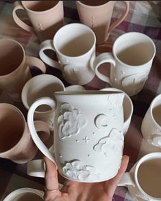 a hand holding a white coffee mug surrounded by cups