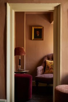 a living room with a chair, lamp and painting on the wall above it's doorway