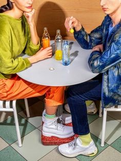 two people sitting at a table with drinks in front of them, one holding a bottle