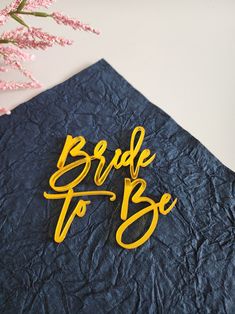 the bride to be sign is next to a pink flower on a blue table cloth