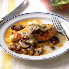 a white plate topped with meat covered in sauce and mushrooms next to a knife and fork