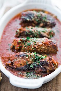 two meats in a red sauce with parsley on top and bread next to it