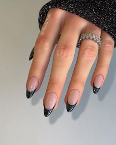 These nails stand out with a sleek black glitter French tip on a nude base, perfect for a bold winter look. The almond shape gives it elegance, while the dark glitter adds a touch of glamour. This design is ideal for anyone looking to blend simplicity with a bit of edge. Silver French Tip Nails Almond, Black Glitter Nails French Tips, Nye Nails Almond Shape, Dark French Tip Nails, Black Glitter French Tip Nails, French Tip Nails Winter, Black Glitter French Tip, Dark Glitter Nails, Winter French Tips