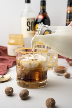 a person pouring milk into a glass filled with ice cream and nuts on top of a table