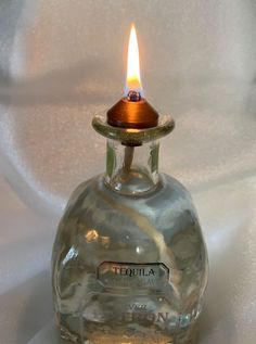 a small glass bottle with a lit candle in it on a white tablecloth background