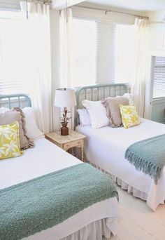 two beds in a room with white walls and green bedding, one has yellow pillows on it