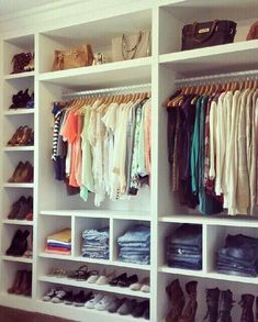 an organized closet with white shelving and lots of clothes hanging on the shelves,