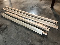 four pieces of wood sitting on top of a cement floor next to a metal pole