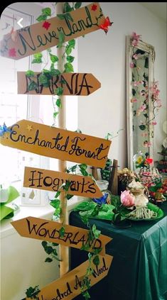 a table topped with lots of wooden signs next to a wall filled with flowers and greenery