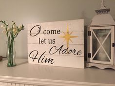 a wooden sign that says, come let us adore him with flowers in a vase