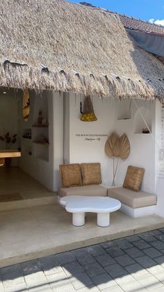 a white couch and table in front of a thatched roof hut with wicker accents