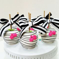 three decorated apples with black and white stripes, pink roses and bows on them are sitting on a plate