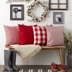 a bench with some red and white pillows on it next to a wall with pictures