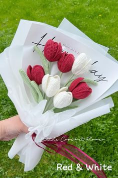 a hand holding a bouquet of red and white crocheted tulips on top of paper