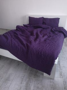 a bed with purple sheets and pillows on it