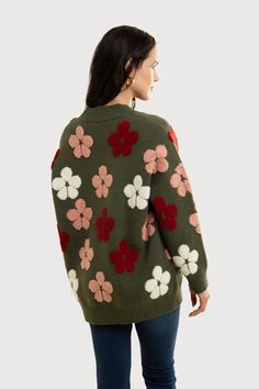 a woman is wearing a green sweater with flowers on the front and back, she has her hands in her pockets