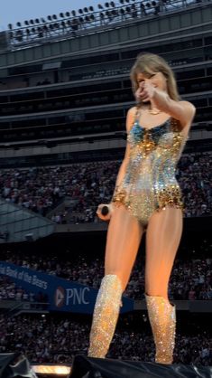 a woman in gold outfit on stage at a sporting event with people watching from the bleachers