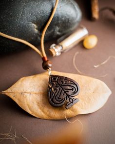 a wooden pendant with an intricate design on top of a leaf next to some beads