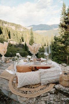 an outdoor table with pillows and vases on it in the middle of a rocky area