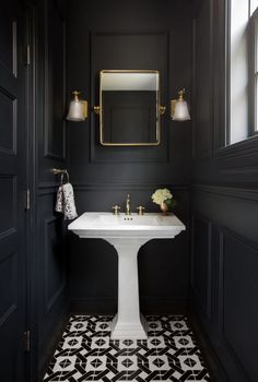 a bathroom with black walls and white pedestal sink in the center, along with gold accents