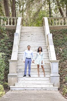 a man and woman standing on the steps in front of some stairs with trees behind them