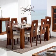 a dining room table and chairs in front of a window overlooking the ocean with an open bookcase