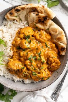 a bowl filled with chicken curry and rice next to pita bread on a table